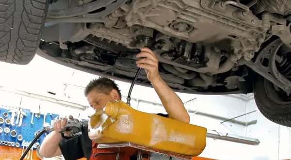 Mechanik wymienia olej w skrzyni biegów DSG, używając żółtego zbiornika i pompy.